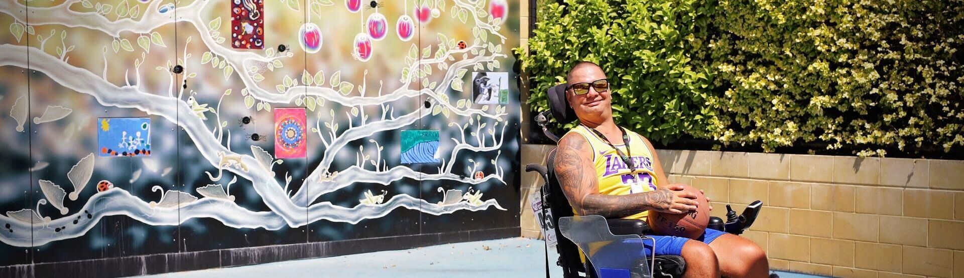 Brightwater Disability NDIS_disability client with Lakers jersey on outside of colourful art graffiti wall