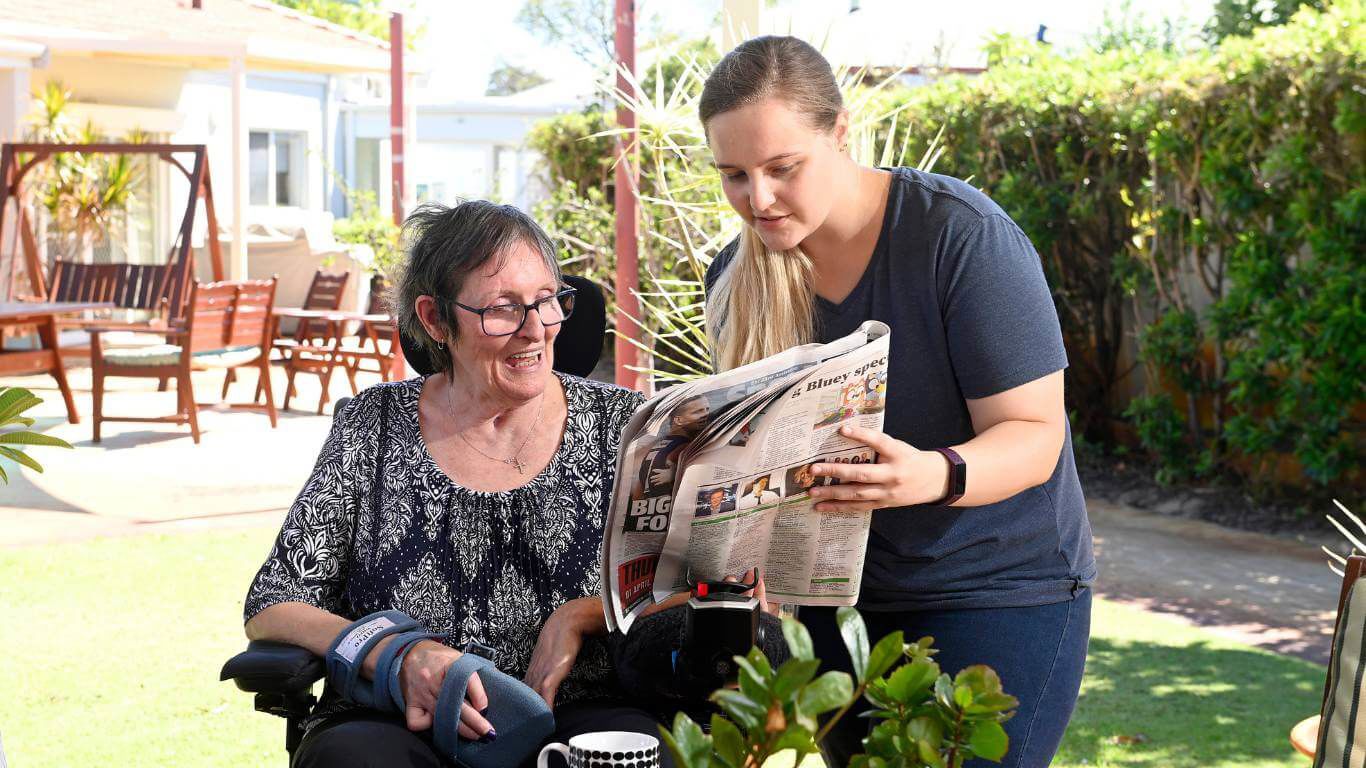 Brightwater Marangaroo Transitional Accommodation Program_disability client in outdoor garden reading newspaper with support worker