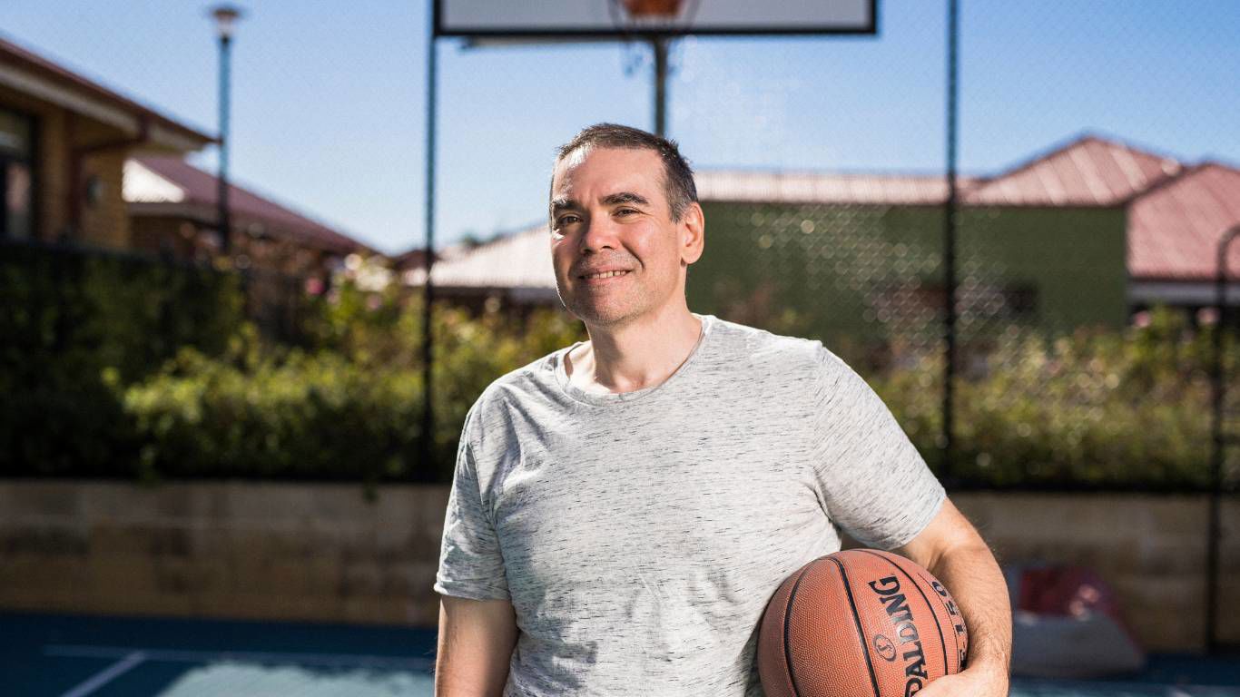 Brightwater Oats Street_disability client smiling with basketball in his hand on the private basketball courtyard